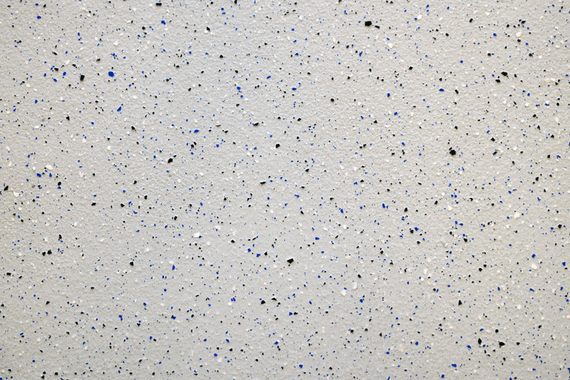 Graue Wand mit blauen und schwarzen Farbsprenkeln.